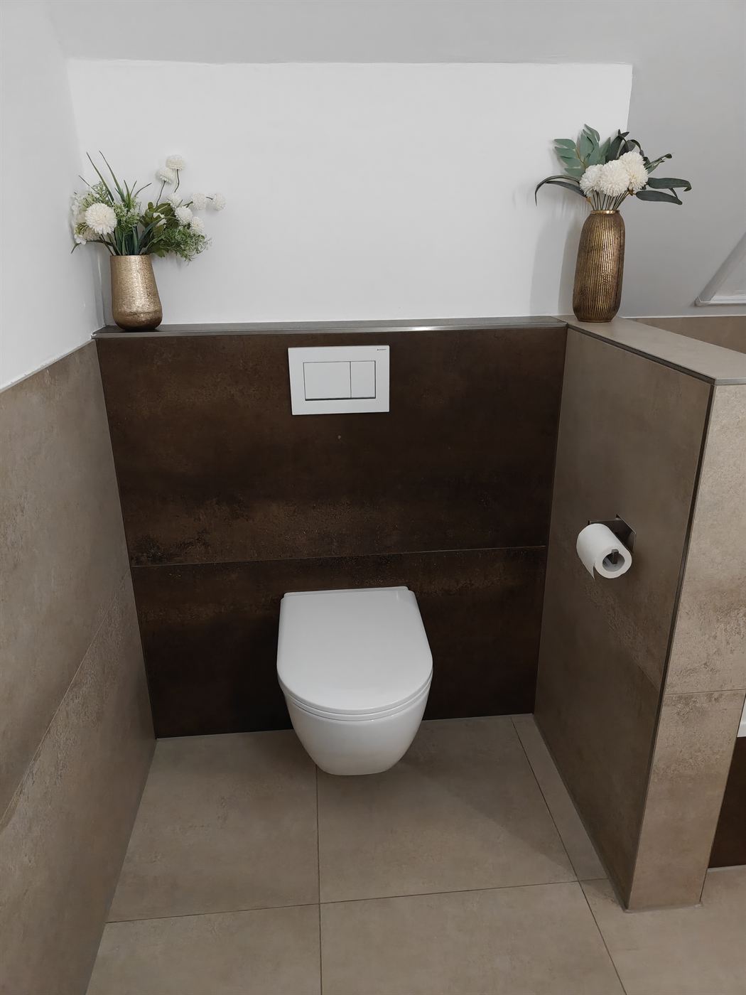 Wandhängendes WC vor einer Vorwand mit Fliesen in dunkler Rostoptik und Geberit-Betätigungsplatte